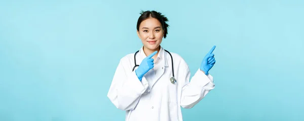 Usmívající Asijský Zdravotnický Pracovník Sobě Sterilní Rukavice Uniformu Ukazuje Vpravo — Stock fotografie