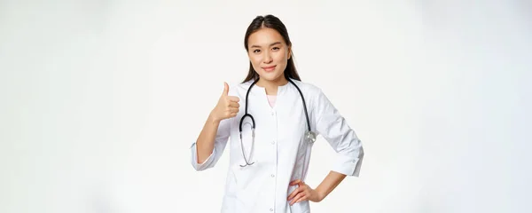 穿着医疗制服的专业医生微笑着露出大拇指 快乐的亚洲女医生证实了口臭 推荐产品 白色背景 — 图库照片
