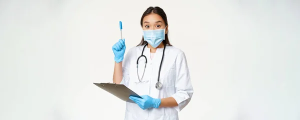 兴奋的女医生 拿着剪贴板 举起钢笔 找到解决方案或想法 戴着医疗面罩站在白底上的亚裔医生 — 图库照片