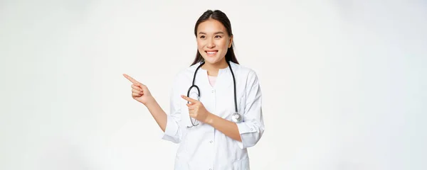Tıbbi Üniformalı Gülümseyen Asyalı Kadın Doktor Parmaklarını Gösterip Reklamlara Bakıyor — Stok fotoğraf