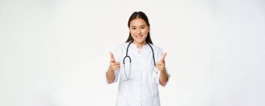 Güzel bayan Asyalı doktor, üniformalı hemşire baş parmağını kaldırıyor ve gülümsüyor..