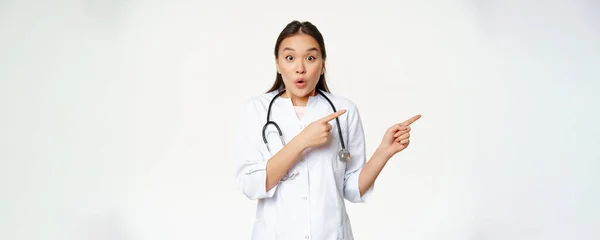 驚くべき女性医師はすごいと言います 右を指して クリニックでの割引で驚いて見て 方法を示します 白い背景に対する医療制服に立って — ストック写真