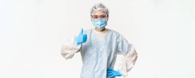 Kişisel koruyucu ekipman ve lastik eldiven takan Asyalı kadın doktor veya hemşire, sağlık maskesi, baş parmak gösterme, aşı ve covid-19 kampanya konsepti.