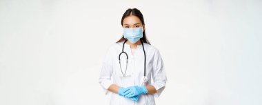 Covid-19 ve sağlık hizmeti konsepti. Tıbbi maskeli genç Asyalı kadın doktor, lastik eldivenler ve klinik üniforması yardım etmeye hazır, dinleyen hasta, beyaz bir geçmişi var..