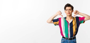 Kötü bir şeyi yargılayan eşcinsel hayal kırıklığına uğramış, baş parmaklarını gösteren hoşnutsuzluğu, hoşnutsuzluğu ve itirazı olan, beyaz arka planda duran.