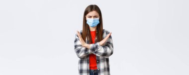 Coronavirus salgını, karantina, sosyal mesafeler ve duygu kavramı. Yeter, bu durmalı. Tıbbi maske takan ciddi şekilde rahatsız genç bir kadın, çapraz işaret göster..