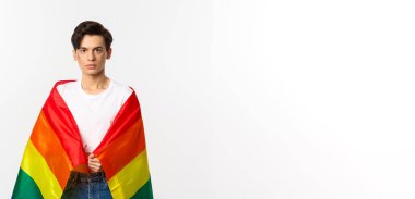 Ciddi görünümlü cinsiyet değişkeni yüzü simli, lgbtq gökkuşağı bayrağı takan, beyaz arka planda duran biri..