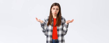 Yaşam tarzı, farklı duygular, boş zaman aktiviteleri konsepti. İsteksiz ve dikkatsiz genç bir kadın ellerini yana açmış omuz silkiyor, bilmiyorum, yardım edemiyorum, hiçbir fikrim yok, beyaz arka planda duruyorum..