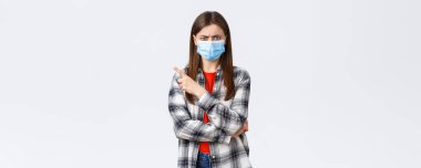 Coronavirus salgını, karantina, sosyal mesafeler ve duygu kavramı. Tıbbi maskeli kızgın ve hayal kırıklığına uğramış genç bir kadın, sol üst köşeyi işaret ediyor, çatık kaşlı bir deli..
