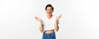 Lgbtq ve gurur konsepti. Mutlu genç eşcinsel adam gülümsüyor, gülüyor ve mutluluktan el çırpıyor, beyaz arka plana karşı mahsulün tepesinde dururken seviniyor..