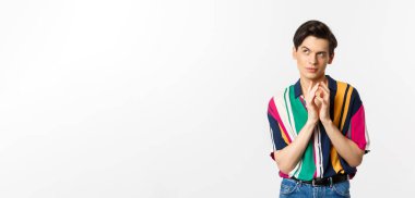 Sinsi genç adamın bir planı var. Çan kulesi gibi parmakları var ve sol üst köşede kurnaz görünüyor. Bir şeyler planlıyor, beyaz arka planda duruyor..