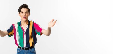 Şaşırmış genç yakışıklı adam ellerini öne uzatıyor, bir şeyi tutmak ya da almak istiyor, arzuyla bakıyor, beyaz arka planda duruyor..