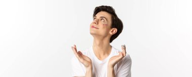 Millet, lgbtq ve güzellik konsepti. Yakışıklı, çift cinsiyetli, yüzünde parıltı ve tırnaklarında parlaklık olan hayaller kuran, gülümseyen, beyaz bir arka planı olan adamın yakın çekimi..
