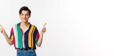 Yakışıklı tuhaf adam parmaklarını yana doğru gösteriyor, gülümsüyor memnun ve iki seçenek gösteriyor, beyaz arka planda duruyor..