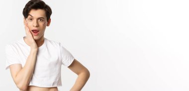 Millet, lgbtq ve güzellik konsepti. Yüzünde sim olan küstah ibne kameraya bakıyor, elleriyle yüzüne dokunuyor, beyaz arka planda duruyor..