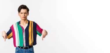 Şüpheci ve hoşnutsuz ibne adam parmaklarını eğip, kötü bir şeyi eleştiriyor ve beyaz arka planda duruyor..