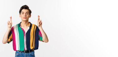 Umut dolu genç çift cinsiyetli adam şans diliyor, dilek tutuyor, bir şey bekliyor, beyaz arka planda duruyor..