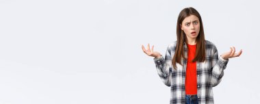 Yaşam tarzı, farklı duygular, boş zaman aktiviteleri konsepti. Hüsrana uğramış ve kafası karışmış genç bir kadın cevaplar istiyor. Elleri yana açık omuz silkiyor. Kameraya bakıyor..