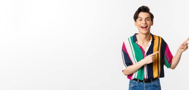 Mutlu gay adam gülüyor ve gülümsüyor, tanıtım teklifini işaret ediyor, beyaz arka planda duruyor. Boşluğu kopyala