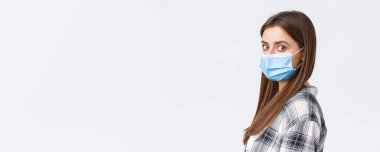 Coronavirus salgını, karantina, sosyal mesafeler ve duygu kavramı. Ciddi genç ve çekici bir kadının profil fotoğrafı. Tıp maskeli bir öğrenci. Kameraya dön..