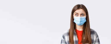 Coronavirus salgını, karantina, sosyal mesafeler ve duygu kavramı. Tıbbi maskeli kafası karışmış ve ürkmüş bir kız garip bir şey gördüğünde, kaşlarını kuşkulandırır..