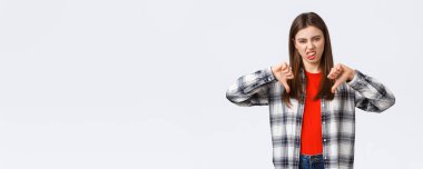 Yaşam tarzı, farklı duygular, boş zaman aktiviteleri konsepti. Hoşnutsuz ve etkilenmemiş, seçici kız işaretli gömlek, baş parmak aşağı ve beğenmediklerini ifade etmek için dilini göster, berbat film derecesi.