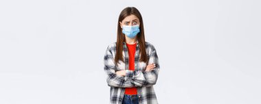 Coronavirus salgını, karantina, sosyal mesafeler ve duygu kavramı. Şok olmuş ve kafası karışmış genç bir kız garip haberler duyuyor, kaşlarını kaldırıyor, tıbbi maske takıyor..