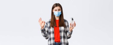 Coronavirus salgını, karantina, sosyal mesafeler ve duygu kavramı. Hiç sorun değil. Tıbbi maskeli hoş kız el dezenfektanı gibi işaret ve göz kırp..