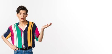 Kafası karışmış eşcinsel adam ne olduğunu soruyor, elini kaldırıyor ve kameraya şaşkın bakıyor, beyaz arka planda duruyor..