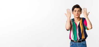 Şok olmuş ve rahatsız olmuş genç bir adam el sıkışıyor ve üzgün görünüyor, beyaz arka planda duruyor..