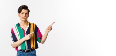 Şüpheci eşcinsel adam hayal kırıklığına uğruyor, kötü ürünü işaret ediyor, beyaz arka planda duruyor..