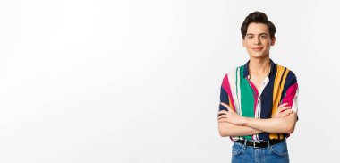 Güzel görünümlü genç adam göğsünde çapraz kollar, kameraya gülümsüyor, beyaz arka planda duruyor..