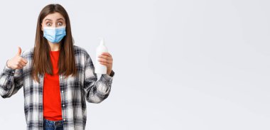 Coronavirus salgını, karantina, sosyal mesafeler ve duygu kavramı. Tıbbi maskeli heyecanlı ve tatmin olmuş bir kız el dezenfektanı, virüs sabununu ve parmak uçlarını önlüyor..