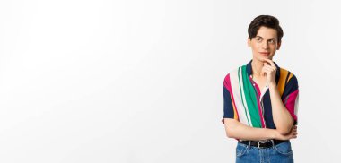 Yaratıcı genç adam düşünüyor ve gülümsüyor, sol üst köşeye bakıyor düşünceli, beyaz arka planda duruyor..