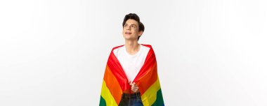 İnsan hakları ve lgbtq toplum kavramı. Yüzünde parıltı olan, gökkuşağı gurur bayrağı takan ve sol üst köşede beyaz arka planda güzel, çift cinsiyetli genç bir adam..