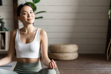 Farkındalık ve meditasyon kavramı. Genç Asyalı kadın evde egzersiz yapıyor. Oturma odasında yoga meditasyonu yapıyor..