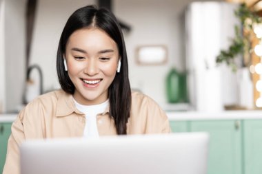 Gülümseyen Asyalı kız dinliyor, dizüstü bilgisayardan izliyor, çevrimiçi Webinar sırasında bilgisayara bakıyor. Uzaktan eğitim veya çalışma kavramı.