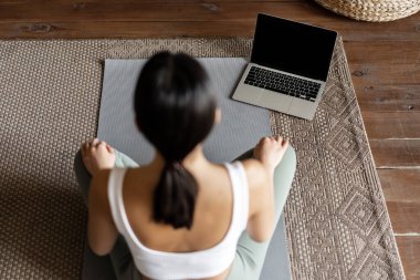 Farkındalık ve meditasyon kavramı. Genç Asyalı kadının evde meditasyon yaparken, dizüstü bilgisayar kursunu takip ederken, oturma odasında paspas üzerinde otururken,.