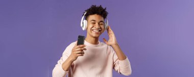 Teknoloji ve yaşam tarzı konsepti. Kaygısız, çekici genç bir adamın portresi. Sesin tadını çıkarıyor, kulaklıkla müzik dinliyor. Harika bir bas kalitesi, cep telefonu var..