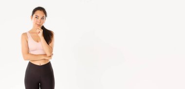 Spor, refah ve aktif yaşam tarzı konsepti. Düşünceli Asyalı fitness kızı, bayan sporcu yeni egzersizler üzerinde düşünüyor, başka tarafa bakıyor, seçim yapıyor, beyaz arka plan.