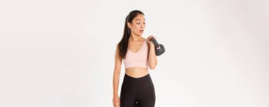 Spor, refah ve aktif yaşam tarzı konsepti. Yakışıklı esmer Asyalı fitness kızı portresi, spor salonunda vücut geliştirme kursuna kaydolma, kettlebell ağırlığı, beyaz arka planda dikilme,.