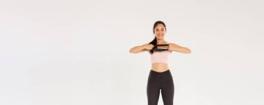 Tam boy ince ve fit görünümlü Asyalı kız spor yapıyor, direnç bandını elleriyle geriyor ve gülümsüyor. Spor salonunda egzersiz malzemesi kullanan antrenör, beyaz arka plan..