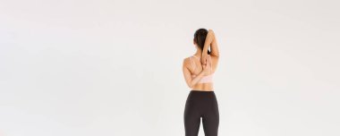 Aktif ve ince esmer Asyalı fitness kızı, yoga derslerinden önce ısınan bayan sporcu, ellerini arkadan kenetle, esneme egzersizleri yapan sporcu kadın, beyaz arka plan..