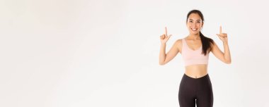 Spor, refah ve aktif yaşam tarzı konsepti. Spor sutyen ve taytlı neşeli, yakışıklı Asyalı sporcu, yukarı bakıyor, gülümsüyor memnun, iyi bir tanıtım teklifi buldu..