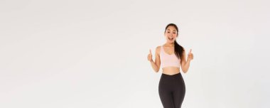 Şaşırmış ve tatmin olmuş bir şekilde gülümseyen fitness kızı, aktif giyinen bayan sporcu yeni spor salonunu ya da egzersiz programını seviyor, baş parmaklarını gösteriyor, antrenmanlara başlamaya teşvik ediyor ya da egzersiz yapıyor..