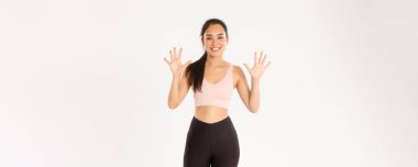 Spor, refah ve aktif yaşam tarzı konsepti. Gülümseyen güçlü ve zayıf Asyalı bayan fitness eğitmeni mükemmel vücut ve üretken çalışma için on adımı açıkla, beyaz arka plan.