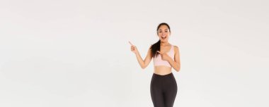 Tam boy arsız çekici bayan sporcu, spor giyimli Asyalı fitness kızı sağ üst köşeyi işaret ediyor, tanıtım yapıyor, egzersiz malzemeleri satışı, fitness eğitimi indirimi gösteriyor..
