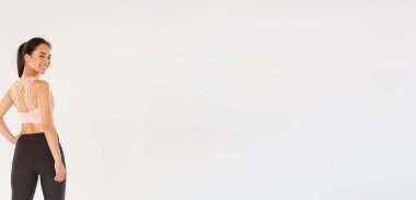 Tam boy gülümseyen ince ve güçlü kadın fitness koçu, spor giyim dalında bayan sporcu arkana dön ve kameraya mutlu, motive olmuş bir ifadeyle bak, çalışmaya hazır bir kız, beyaz bir arka plan..