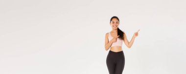 Gülümseyen, spor giyimli, zayıf Asyalı güzel bir kız, sağ üst köşeyi işaret ediyor, spor salonu üyeliği için davet ediyor, egzersiz teklifi sunuyor, fitness koçu sağlıklı diyet önerileri gösteriyor..