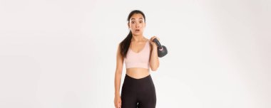 Spor, refah ve aktif yaşam tarzı konsepti. Yakışıklı esmer Asyalı fitness kızı portresi, spor salonunda vücut geliştirme kursuna kaydolma, kettlebell ağırlığı, beyaz arka planda dikilme,.